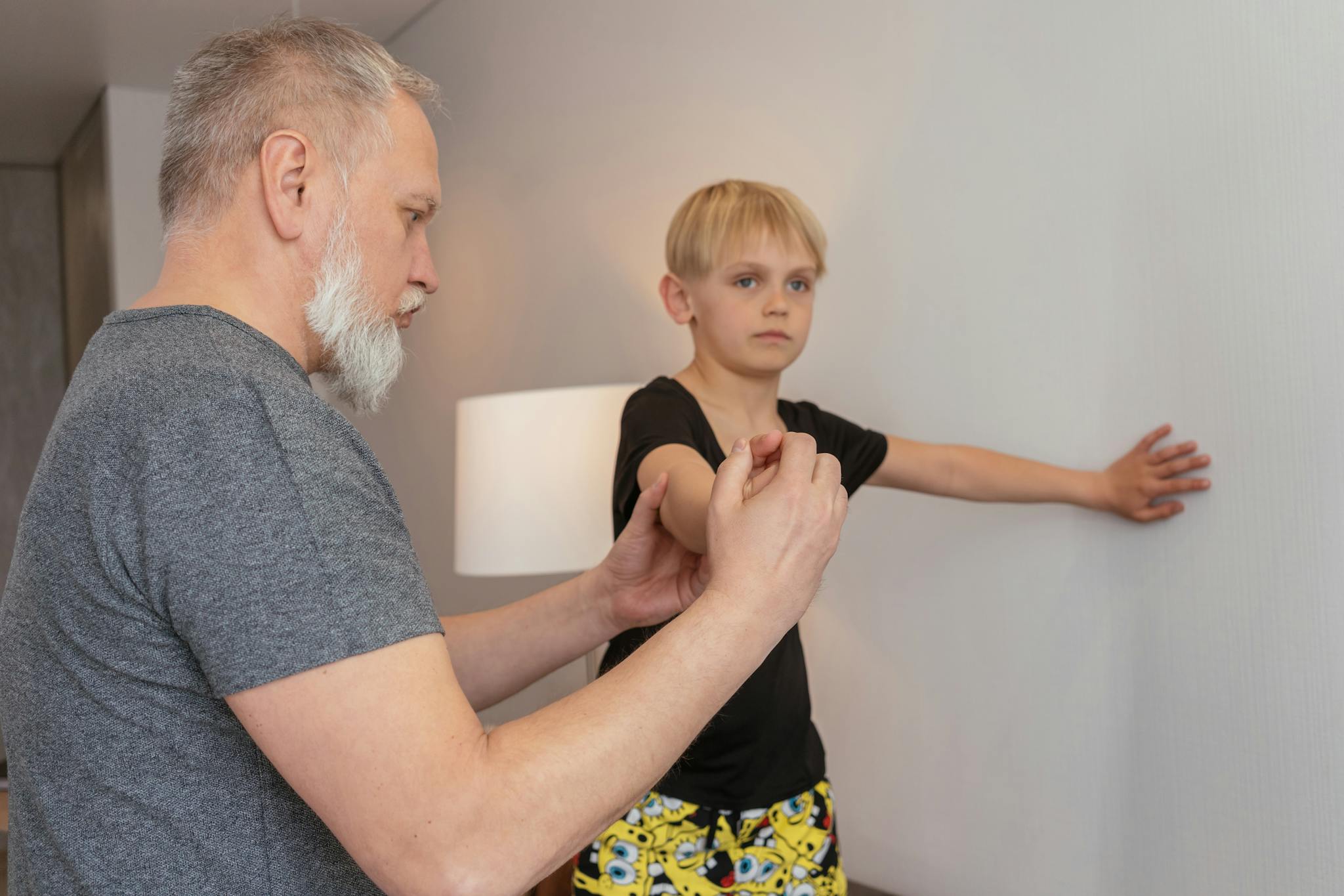 A grandfather guiding his grandson in physical exercise at home for a healthy lifestyle.